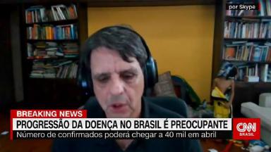 Homem dá entrevista para a CNN Brasil, enquanto ao fundo criança aparece enrolada em toalha do Picachu e usa máscara de herói 