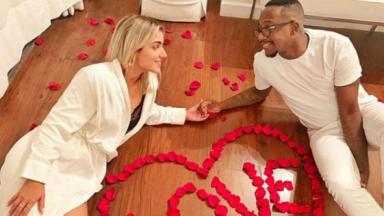 Mumuzinho e Thainá Fernandes segurando a mão um do outro ao lado de um coração de pétalas de rosas escrito a palavra love 
