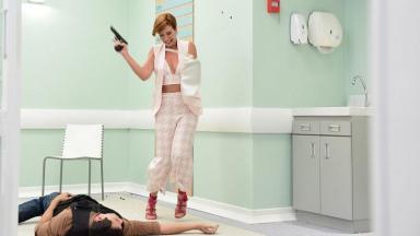Cena da novela "Topíssima" em que Sophia (Camila Rodrigues) segura uma arma e vê um bandido caído no chão do hospital 