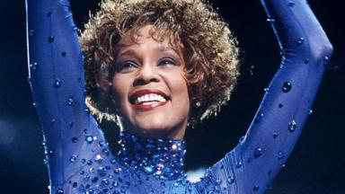 A cantora Whitney Houston levantando as mãos 