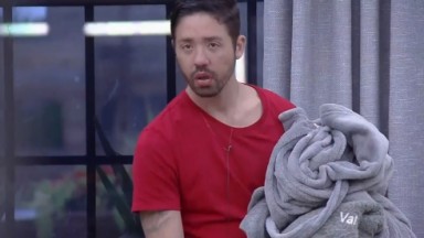 Rico Melquuiades com um cobertor na mão, no momento em que encontra sua jaqueta rasgada em uma cadeira na sede de A Fazenda 