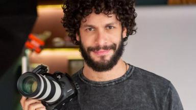 O ator Rainer Cadete com uma máquina fotográfica na mão 
