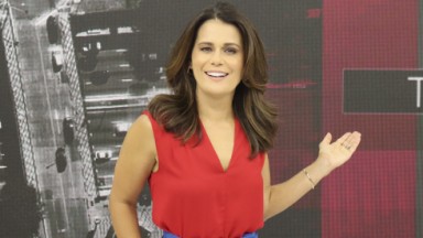 Adriana Araújo sorrindo e usando uma camisa vermelha à frente do Boa Tarde São Paulo na Band 