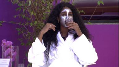 Camilla sentada de roupão e máscara no rosto 