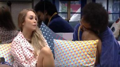 Carla está na sala sentada ao lado de João Luiz 