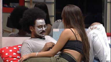 Na sala, João Luiz está com máscara no rosto e conversa com Thaís 