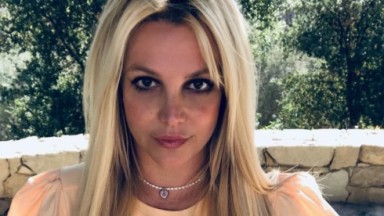 Britney Spears olhando pra câmera com árvores ao fundo 
