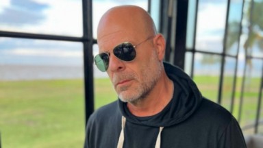Bruce Willis cabisbaixo de óculos de sol  