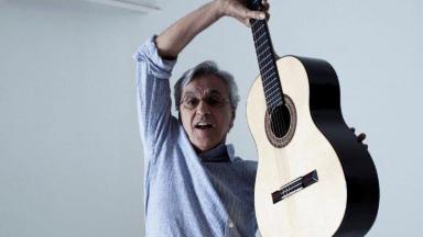Caetano Veloso posado para foto segurando um violão no ar 