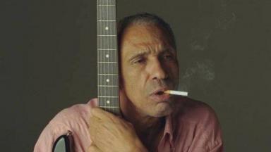 Cantor Cassiano agarrado em sua guitarra, fumando cigarro 