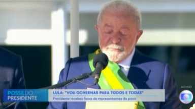 Lula com faixa presidencial, segurando papel e falando em microfone 