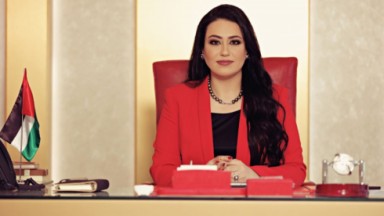 Nashwa Al-Ruwaini de blazer vermelho e blusa preta, com cabelos soltos, sentada 