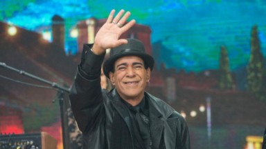 Elymar Santos acenando e sorrindo de roupas pretas no estúdio do Faustão na Band 