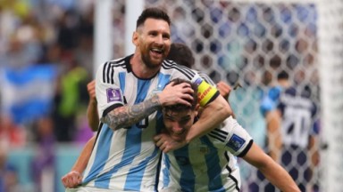 Messi em campo com uniforme da Argentina brincando com colega de time 