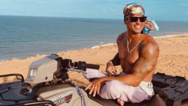 Fernando Fernandes na praia, sentado em cima de moto, com bandana e óculos escuros 