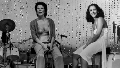Eliz Regina e Gal Costa sentadas em meio a instrumentos musicais e sorrindo em foto em preto e branco 
