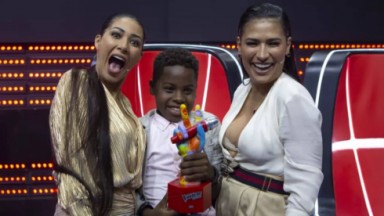  Jeremias Reis com o troféu do The Voice Kids, entre Simone e Simaria no estúdio do programa, os três sorrindo e posando 
