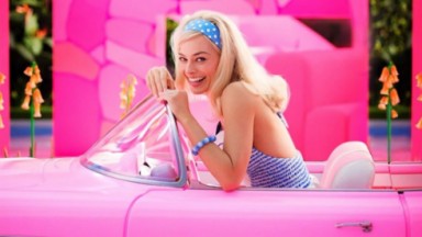  Margot Robbie caracterizada como Barbie sorrindo dentro de um carro conversível rosa 