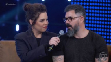 Isabel Teixeira e Juliano Cazarré de roupa preta e falando em microfone no Domingão com Huck 