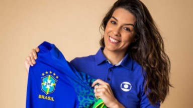 Renata Silveira sorrindo, de cabelos soltos, vestindo camisa da Globo e segurando camisa do Brasil 