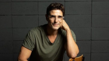 Reynaldo Gianecchini de camiseta verde e óculos, posando apoiado em cadeira 