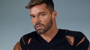 Ricky Martin com expressão séria e posando para foto com camiseta preta rasgada 
