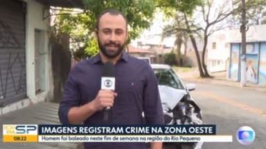 Repórter Rômulo D'Avila falando em microfone da Globo no meio da rua, vestindo camisa social azul marinho 