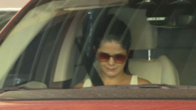 Samara Felippo de cabelo preso e óculos escuros, dentro de carro, de cabeça abaixada 