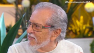 Carlos Alberto de Nóbrega de perfil, de roupa clara e óculos, falando 
