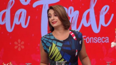 Catia Fonseca de batom vermelho e roupa estampada na frente do telão do Melhor da Tarde 