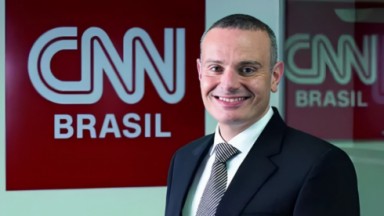 Leandro Cipoloni sorrindo perto de placa da CNN Brasil 