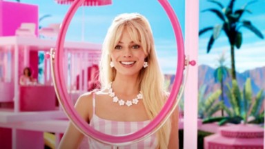 Margot Robbie em cena do filme da Barbie, sorrindo e olhando pra frente 