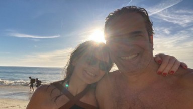 Cláudia Abreu e José Henrique Fonseca posam abraçados em praia 