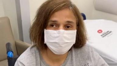 Claudia Rodrigues aparece de máscara, sentada em cadeira de rodas, em quarto de hospital 