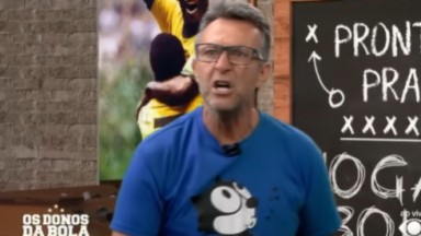 Craque Neto de camiseta azul estampada com desenho e óculos, falando para a câmera com cara de raiva 