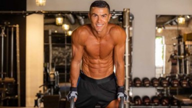 Cristiano Ronaldo sem camisa segurando em dois arcos em uma sala de musculação 