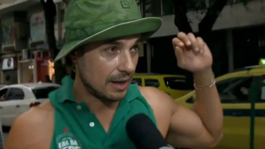 Daniel Erthal de roupa e chapéu verdes, falando e gesticulando 