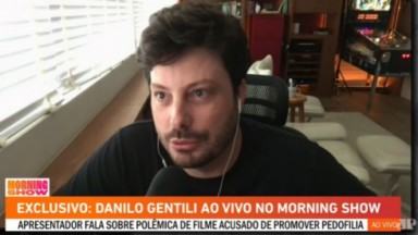 Danilo Gentili de camisa preta e fones de ouvido falando para a câmera 