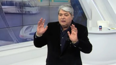 Datena durante Brasil Urgente: ele usa terno preto e levanta as duas mãos  