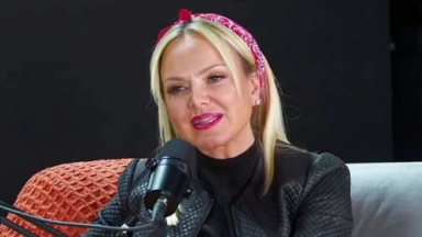 Eliana em entrevista ao podcast O Pod é Nosso. A apresentadora fala ao microfone, usa uma jaqueta preta e está com os cabelos presos por um laço cor-de-rosa 