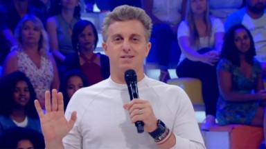 Luciano Huck falando e gesticulando, de blusa branca, perto de plateia da Globo 