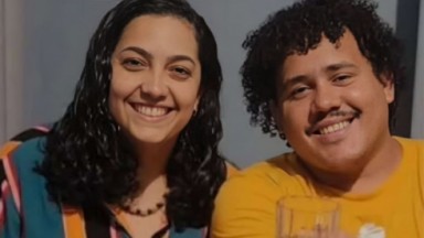 Camila Moura e Lucas Henrique sorrindo, lado a lado em foto, olhando para a câmera 