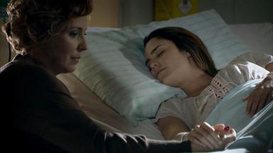 Cena de A Vida da Gente com Ana deitada na cama do hospital de mãos dadas com Eva, que está sentada 