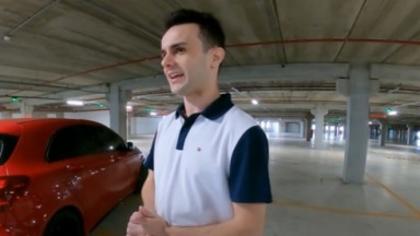 Guillermo Hundadze em garagem, perto de carro vermelho, falando, com camisa polo branca e azul marinho 
