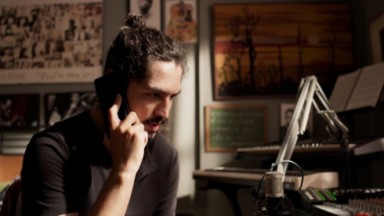 Gabriel Leone como Felipe em cena de Um Lugar ao Sol, de camisa preta, segurando telefone 