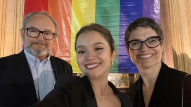 Elisa com os pais, Ernesto Paglia e Sandra Annenberg, com bandeira LGBT atrás 
