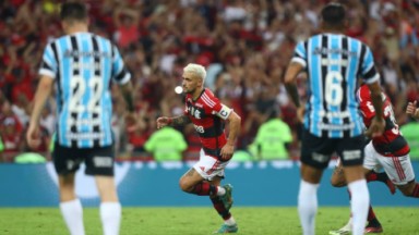 Arrascaeta comemorando gol e jogadores do Grêmio olhando 