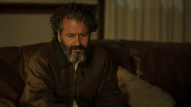 Marcos Palmeira como José Leôncio na novela Pantanal. Ele está sentado no sofá da sala da fazenda 