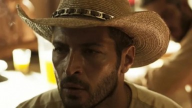 Leandro Lima em cena na novela Pantanal como Levi. O personagem está de chapéu e sentado na fazenda 