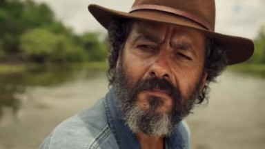Marcos Palmeira como José Leôncio em Pantanal. Ele está sentado perto do rio 